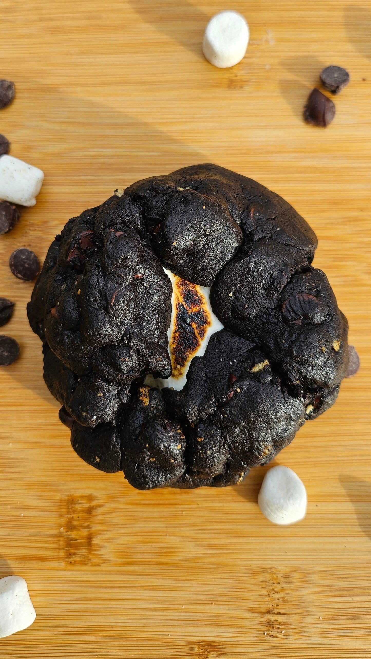 "Freshly baked black velvet s'mores cookies with a soft, dark chocolate center, melted marshmallows, and crispy graham cracker bits."