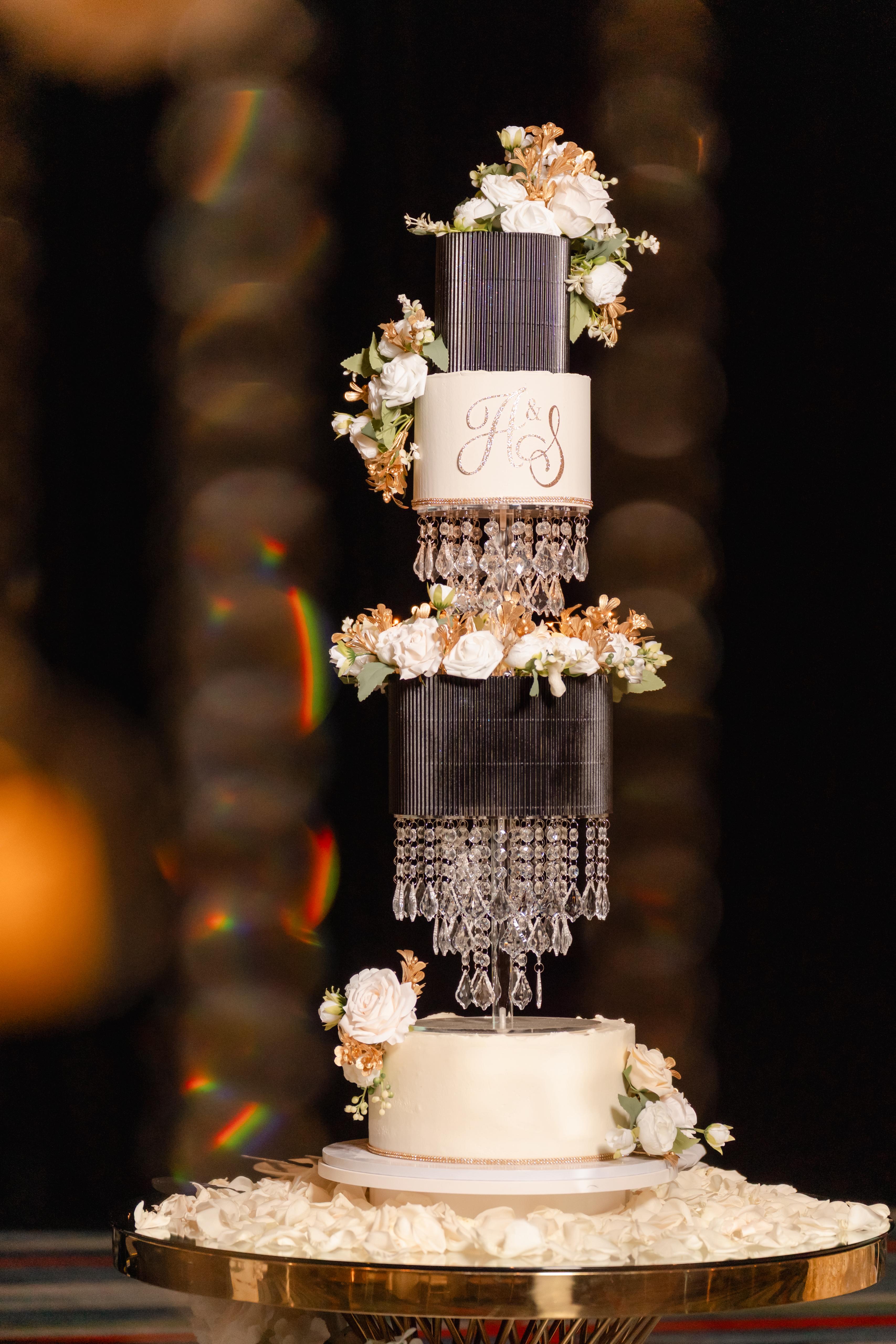 Elegant multi-tier wedding cake with crystal chandelier pillars, white roses, and gold accents on rose petals, Rose Hill Cakes Sanford FL